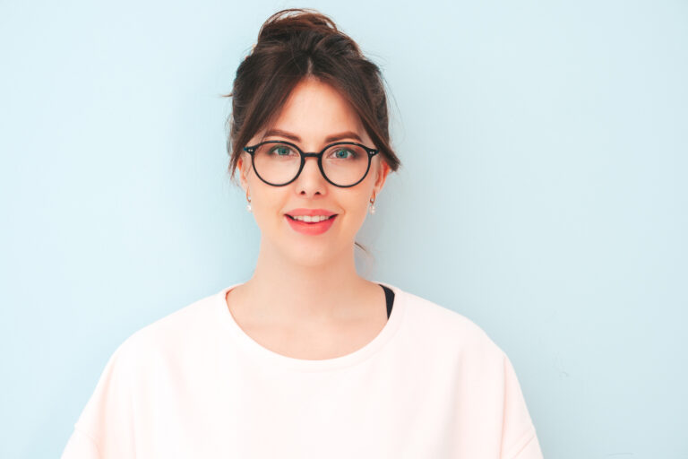 Young beautiful smiling female in trendy summer hipster clothes. Sexy carefree woman posing near light blue wall in studio. Positive model having fun indoors